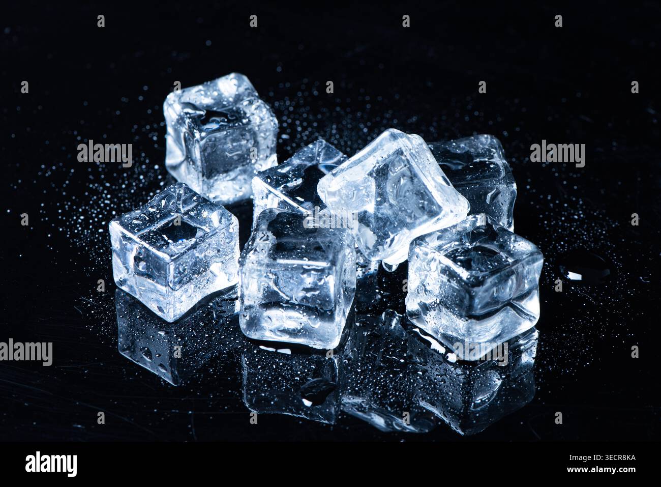 Ice cubes melting on a reflective black surface creating water drops Stock Photo