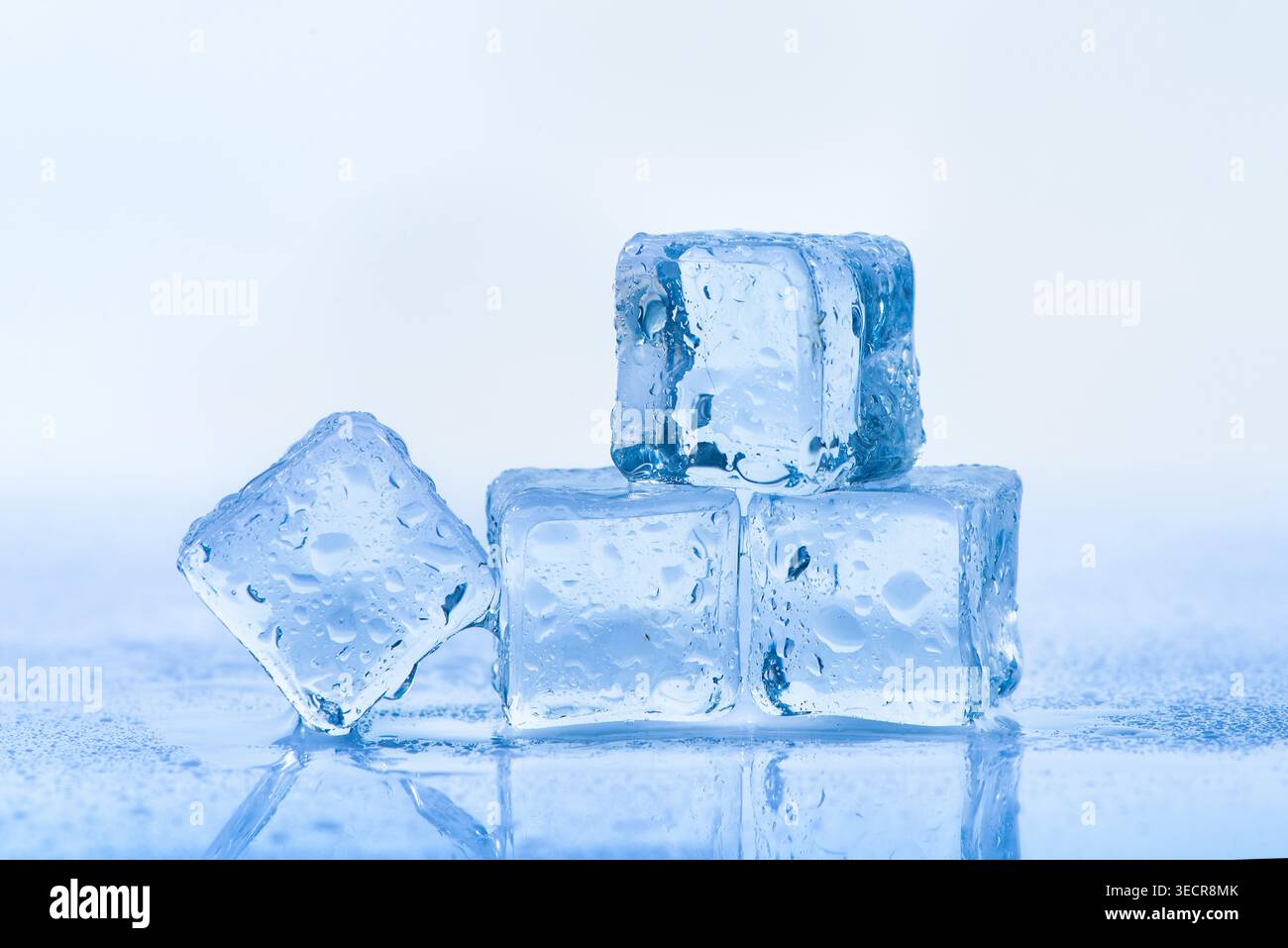 Ice cubes melting on a reflective surface, creating water droplets Stock Photo