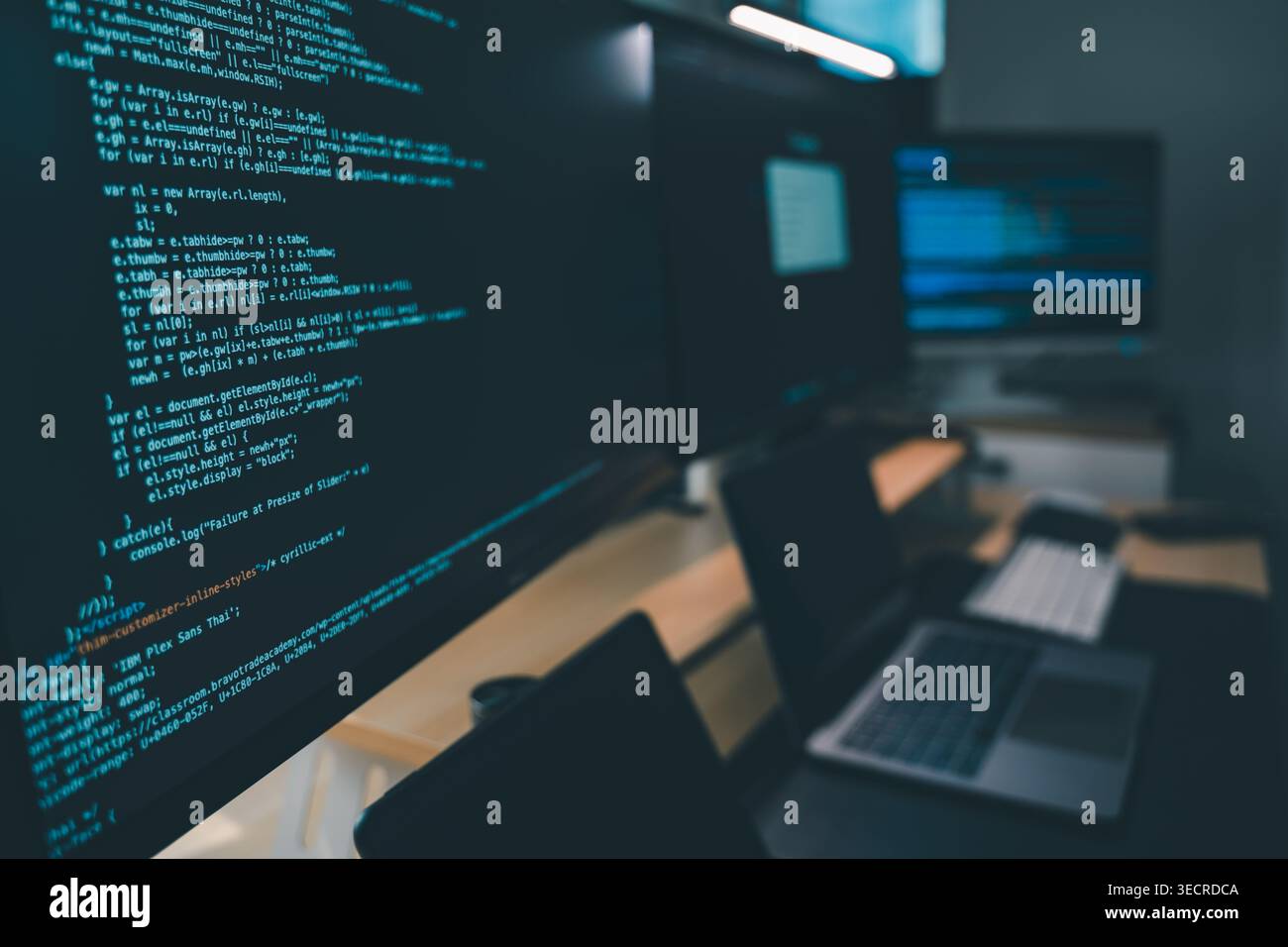 Close up of computer monitors displaying source code in a modern workstation with laptop and digital devices, showing software development workflow, p Stock Photo