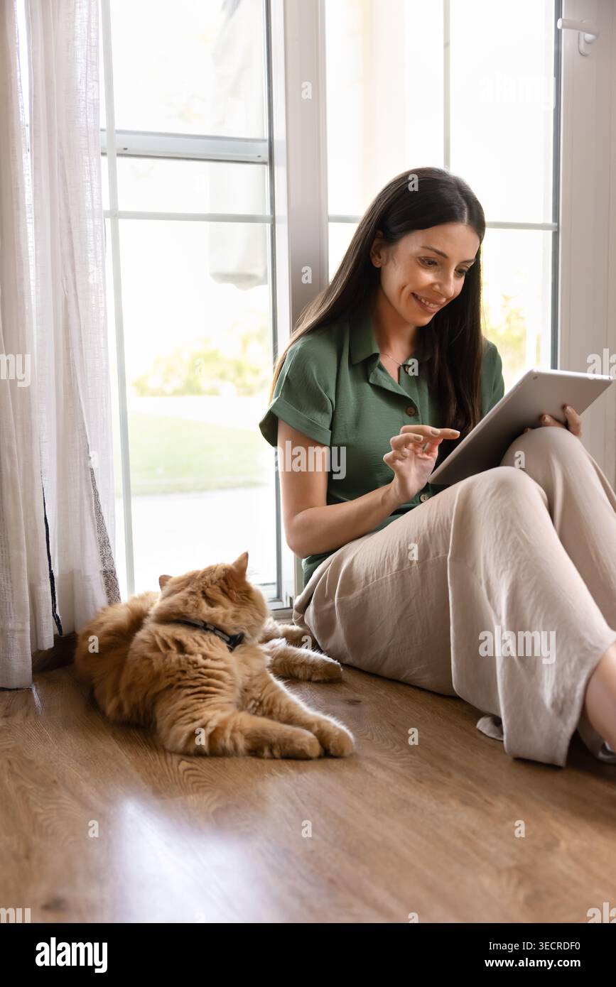 Woman using tablet sitting on floor with cat Stock Photo