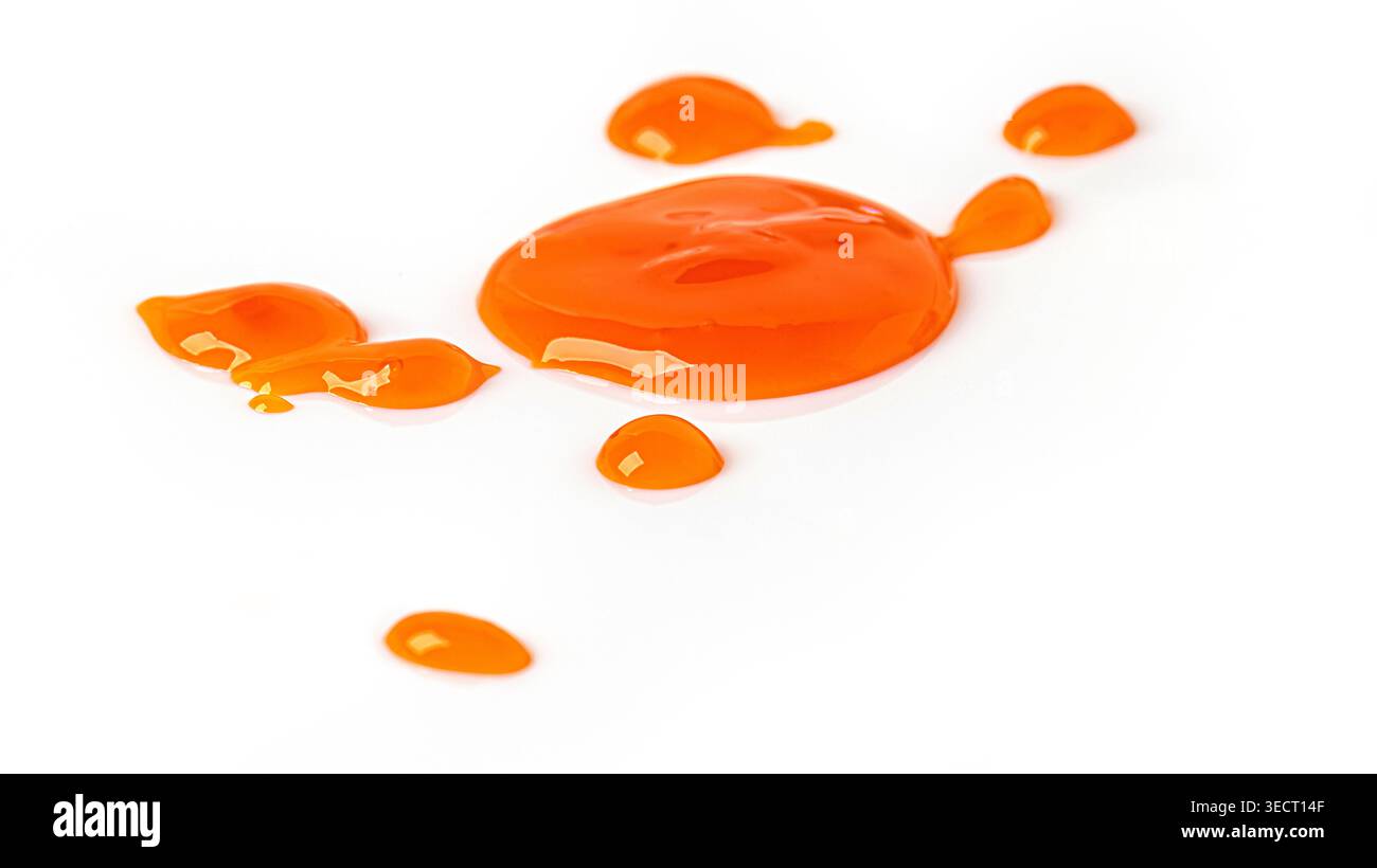 Bright orange liquid dripping and pooling on a clean white surface Stock Photo