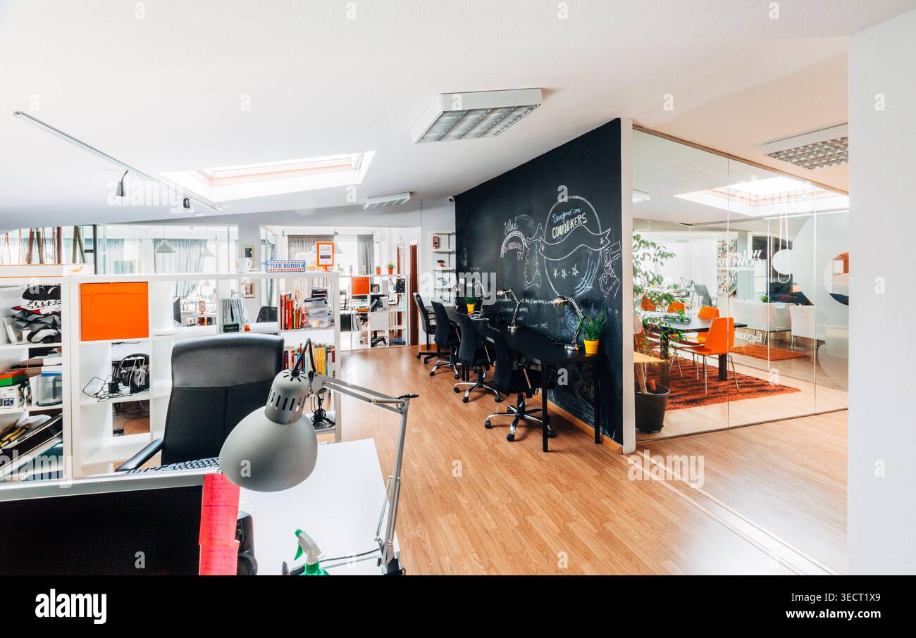 Bright modern open plan office interior with desks, computers and chairs, featuring a black chalkboard wall for brainstorming and a glass meeting room Stock Photo