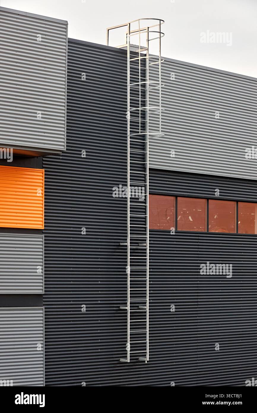 Architectural facade with orange cladding corrugated metal panels, industrial vertical ladder with a safety cage or crinoline, large glass window. Bui Stock Photo