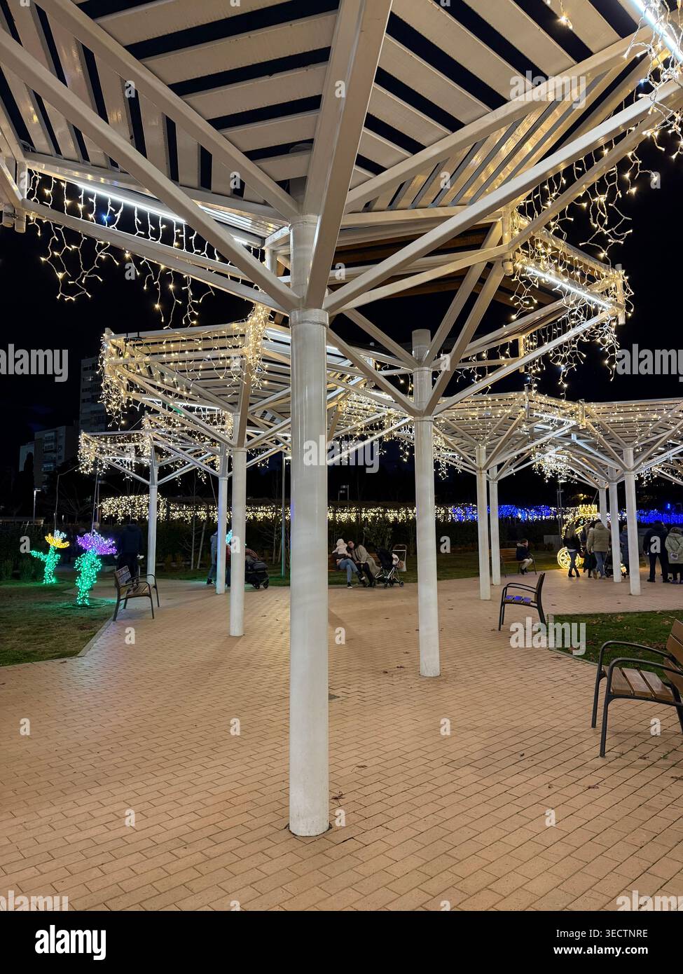 A detailed nighttime photograph in Madrid captures a white timber pavilion intricately adorned with festive Christmas lights within a public park, emp - Smartphone Captured Stock Image