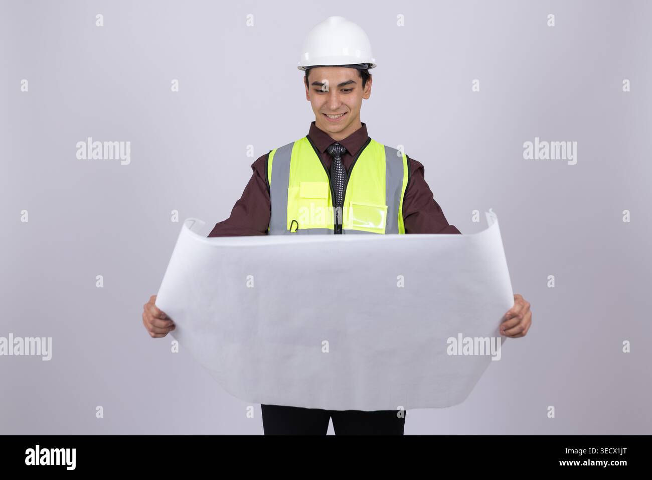Young builder in helmet holding a large white blueprint Stock Photo