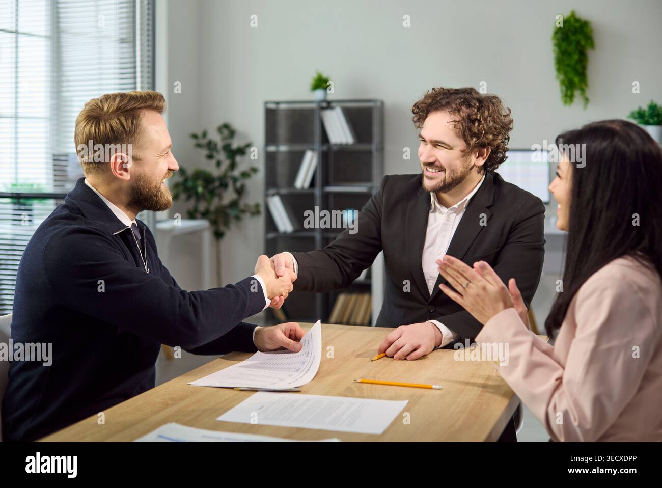 Recruiter and candidate shake hands after interview while colleague applauds Stock Photo
