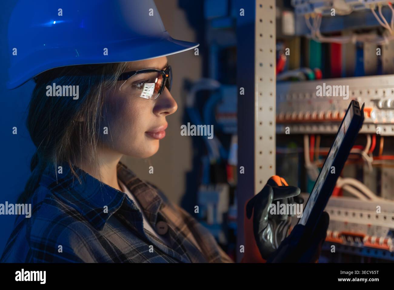 Female electrical engineer inspecting power system on tablet. Digital technical control. Stock Photo
