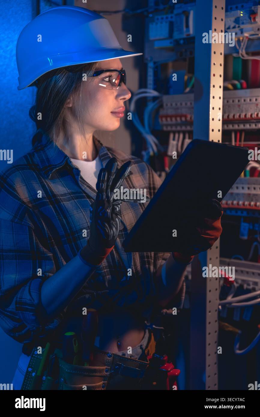 Female electrician inspecting electrical switchboard with tablet device. Modern electrical work. Stock Photo