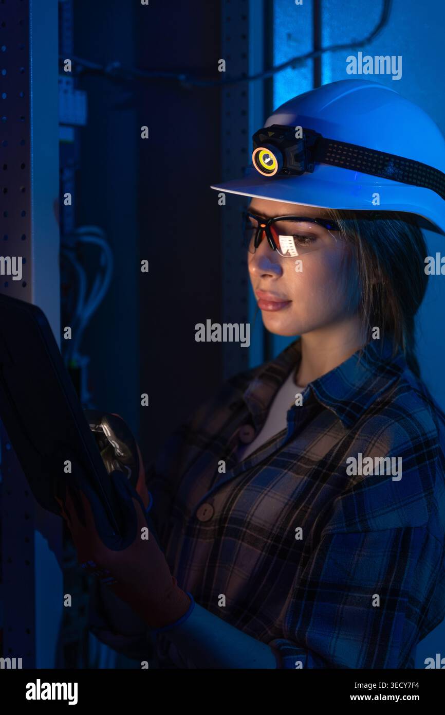 Electrical engineer inspecting power system with tablet near switchboard. Technical control. Stock Photo