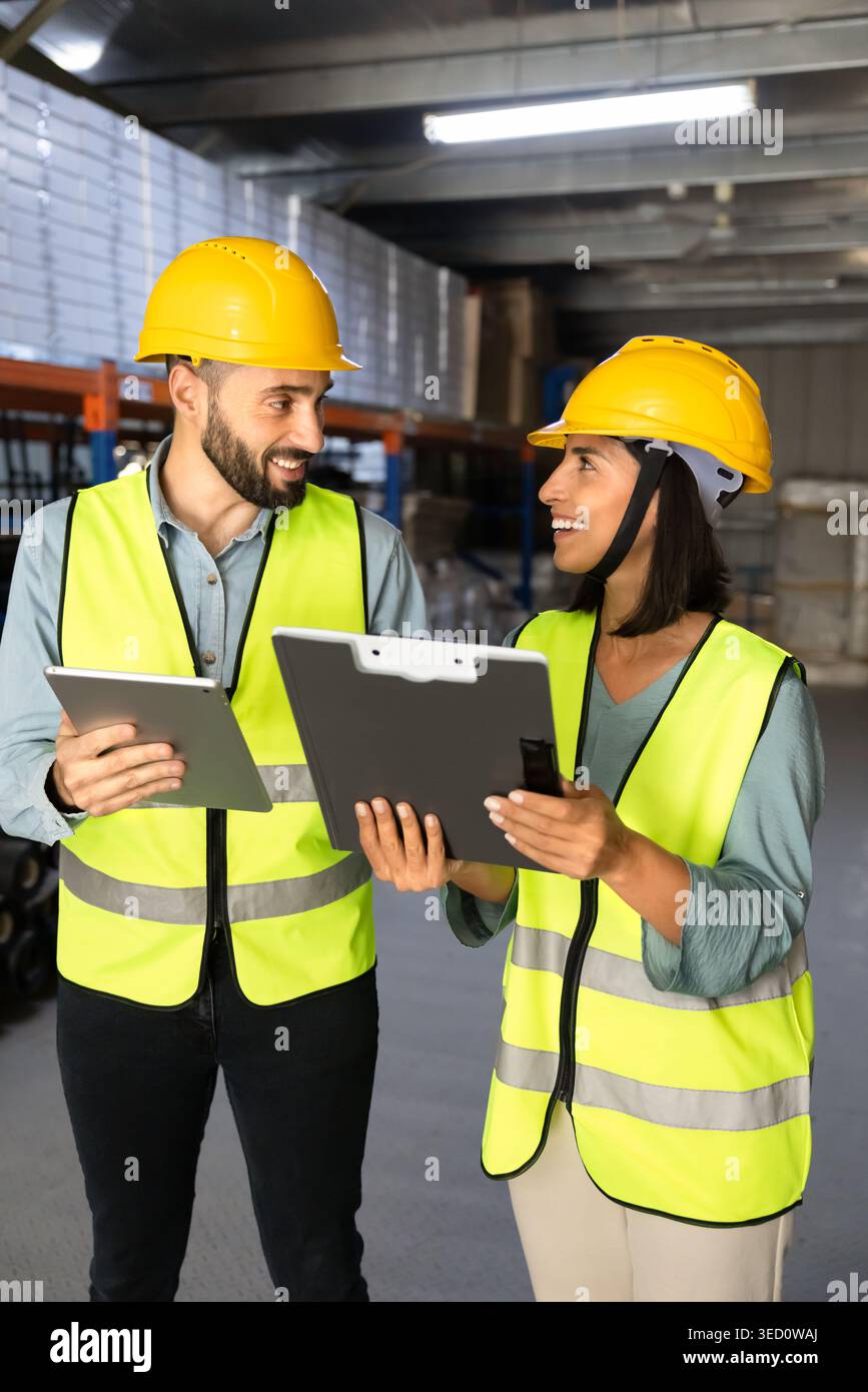 Two workers discussing logistics operations with tablet clipboard in warehouse Stock Photo