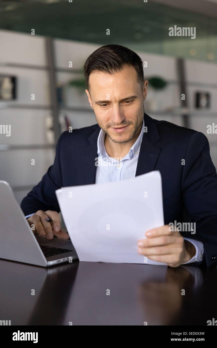 Businessman reviewing printed documents while working on laptop Stock Photo