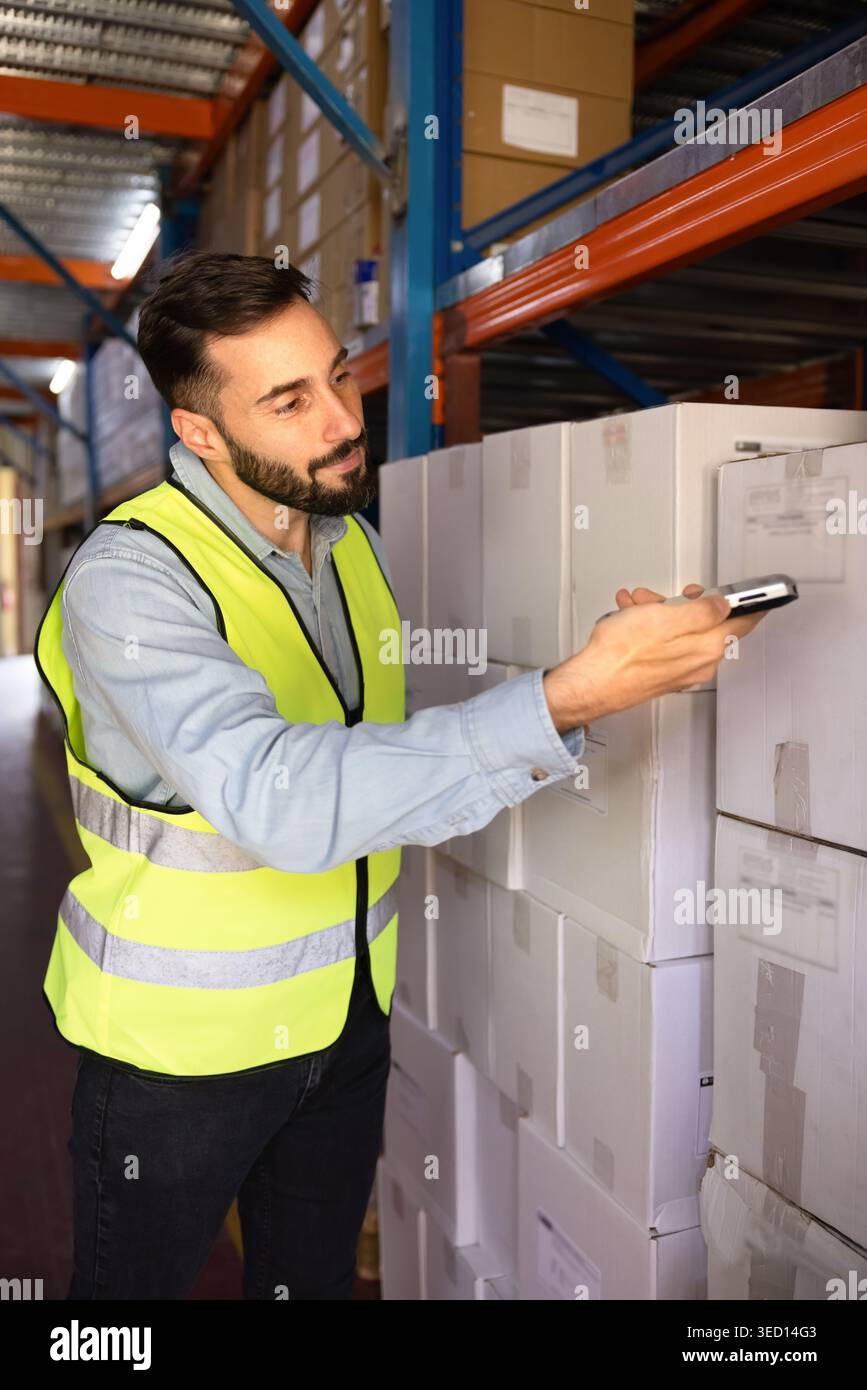 Worker scanning barcode on box stacked in industrial warehouse Stock Photo