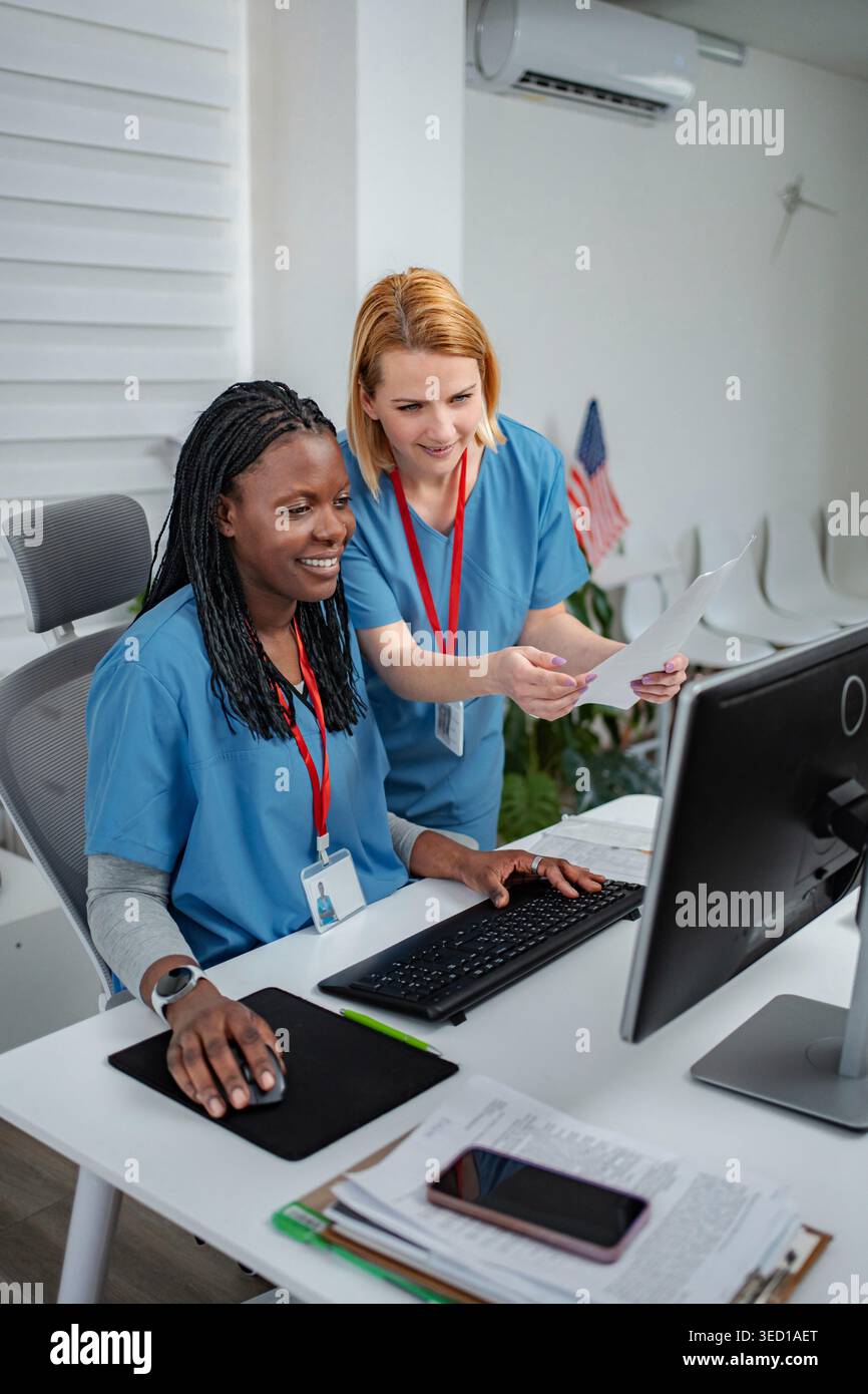 Two female nurses collaborating while looking at a desktop computer screen in a clinic Stock Photo