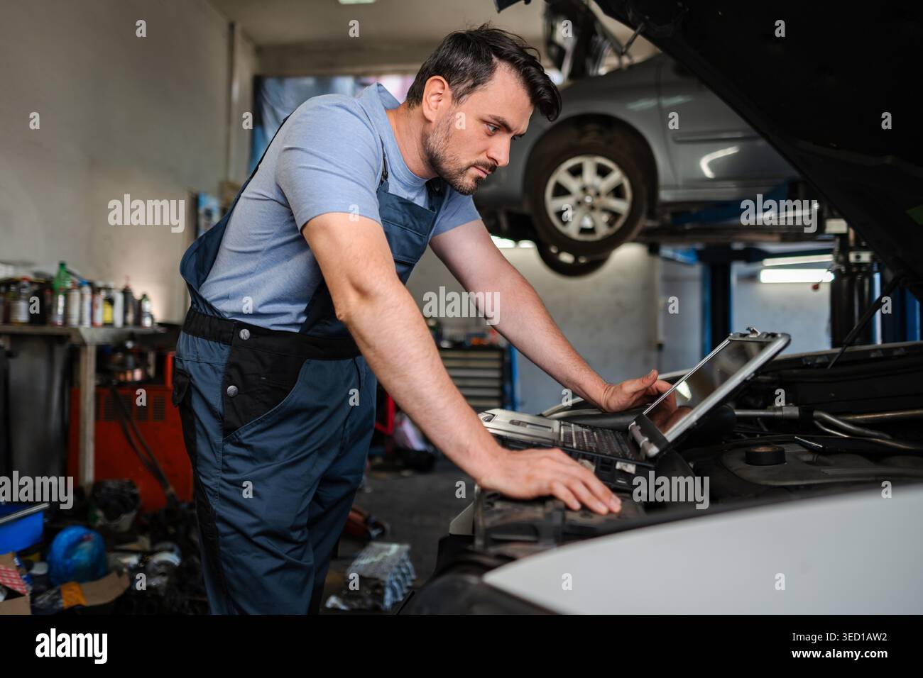 Mechanic using diagnostic software on a laptop to check a car engine in a garage Stock Photo