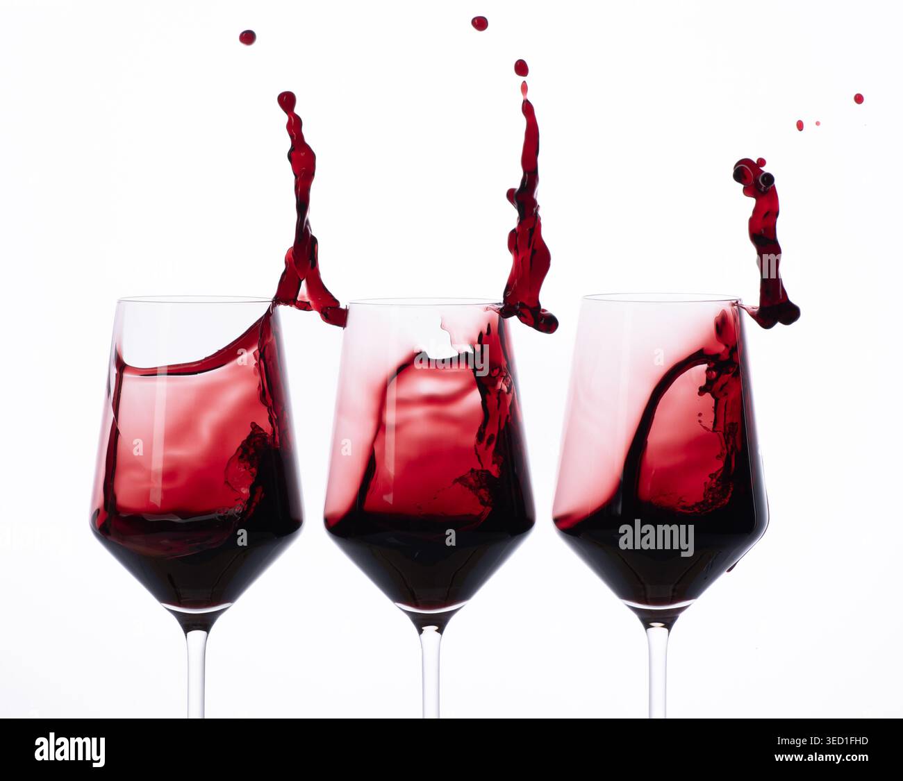Red wine splashes create movement in three glasses in studio. Stock Photo