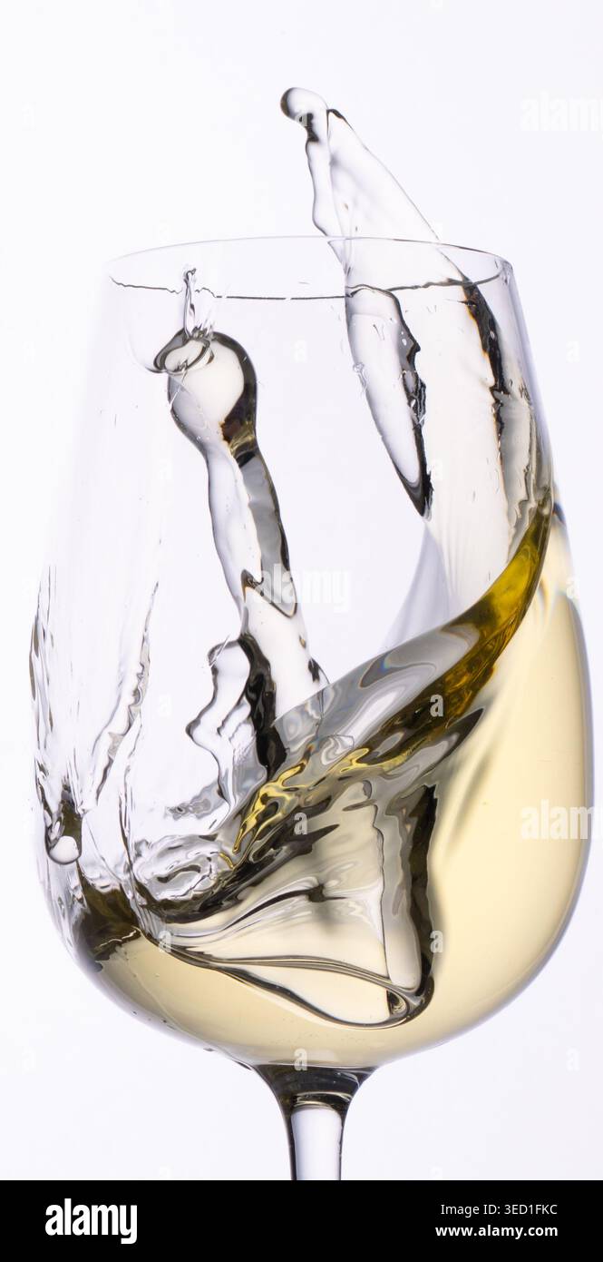 White wine splashes inside a clear wine glass. Stock Photo