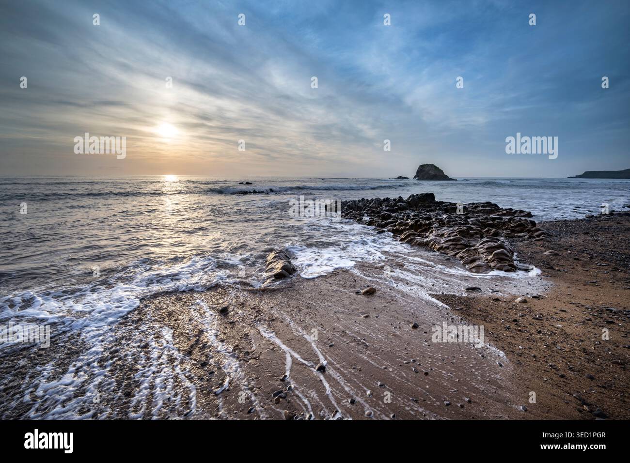 Sun setting behind Black Rock on Widemouth Bay Cornwall viewed at high tide Stock Photo