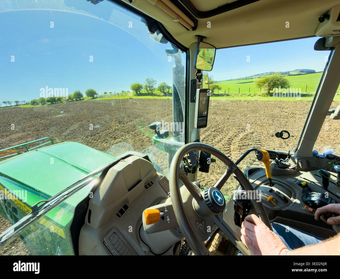 View from the interior cabin of a modern green tractor plowing a field under a clear blue sky - Smartphone Captured Stock Image