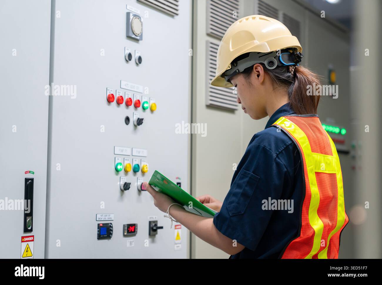 Industrial technician or inspector conducting a safety audit and checking electrical status indicators on a technical control board inside a factory. Stock Photo