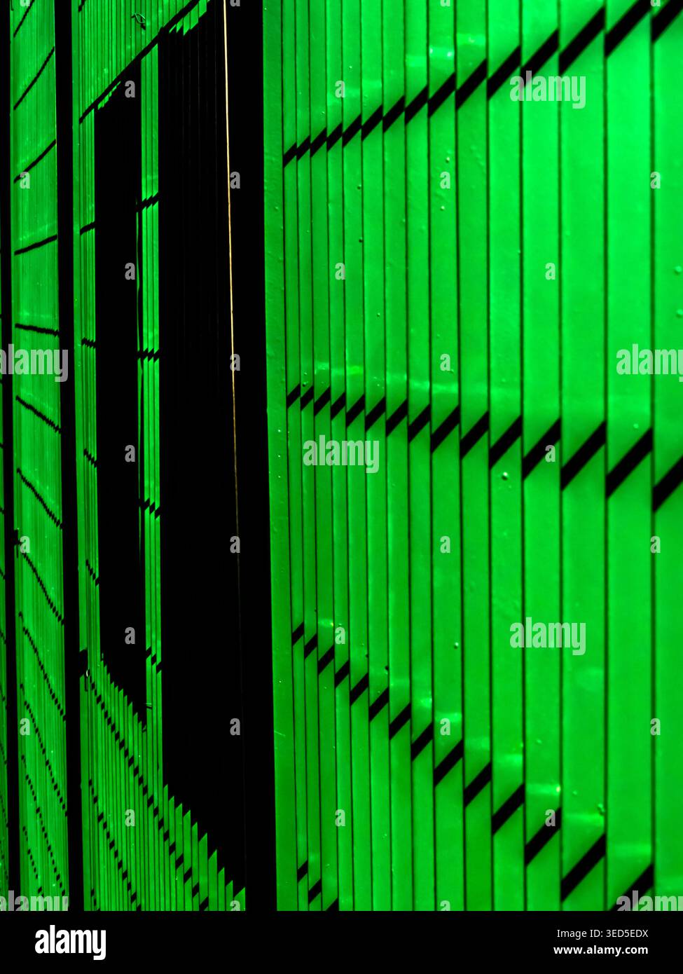Abstract perspective of a vibrant green metal industrial shutter or siding, showcasing clean vertical lines and dark geometric shadows in Brazil. Stock Photo