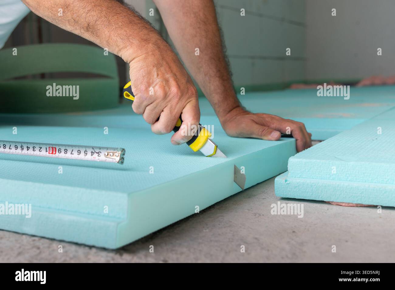 Worker on a construction site, cutting insulation boards before laying and fixing on a concrete floor Stock Photo