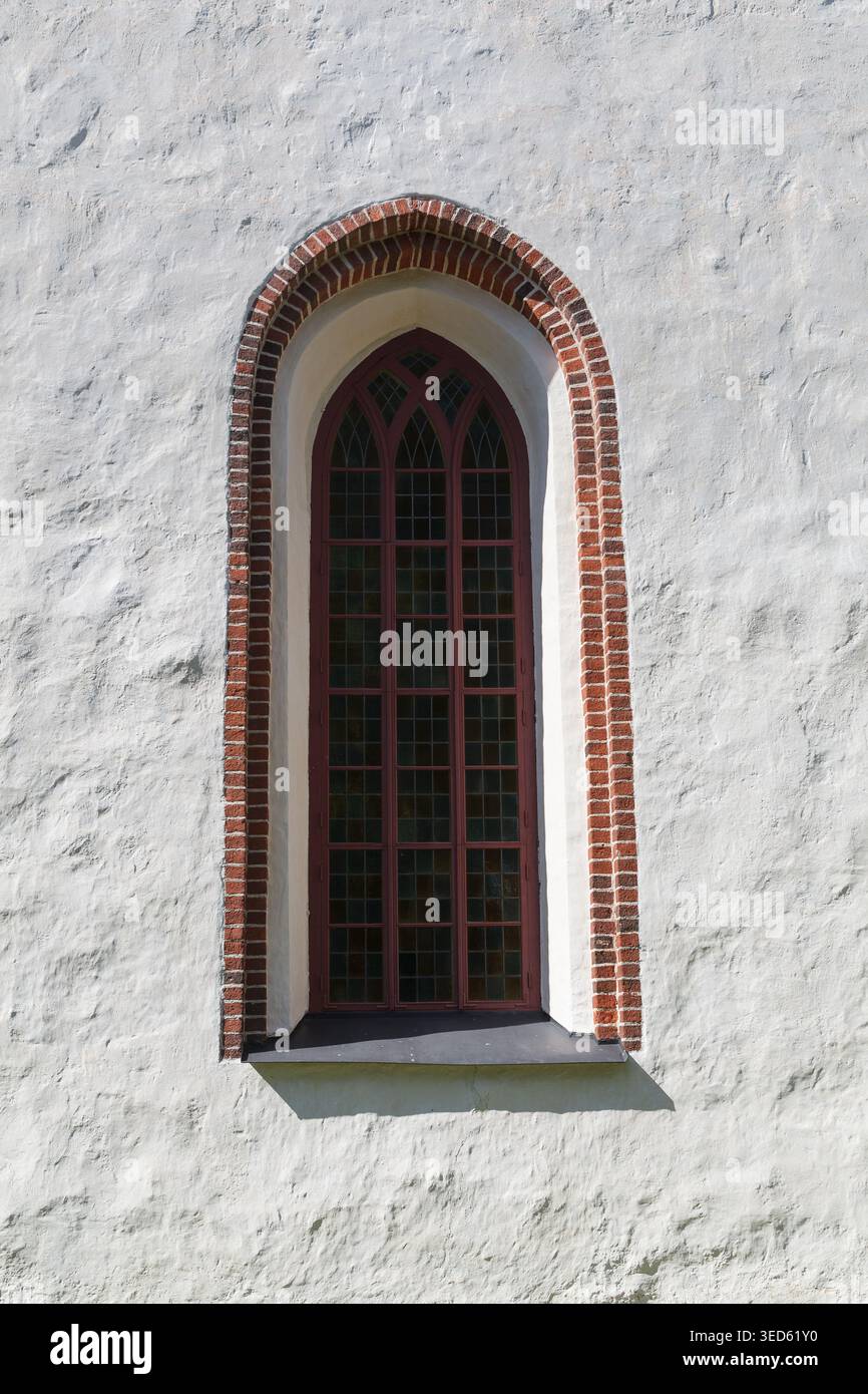 Gothic arched window with red brick frame set in white stone wall of ...