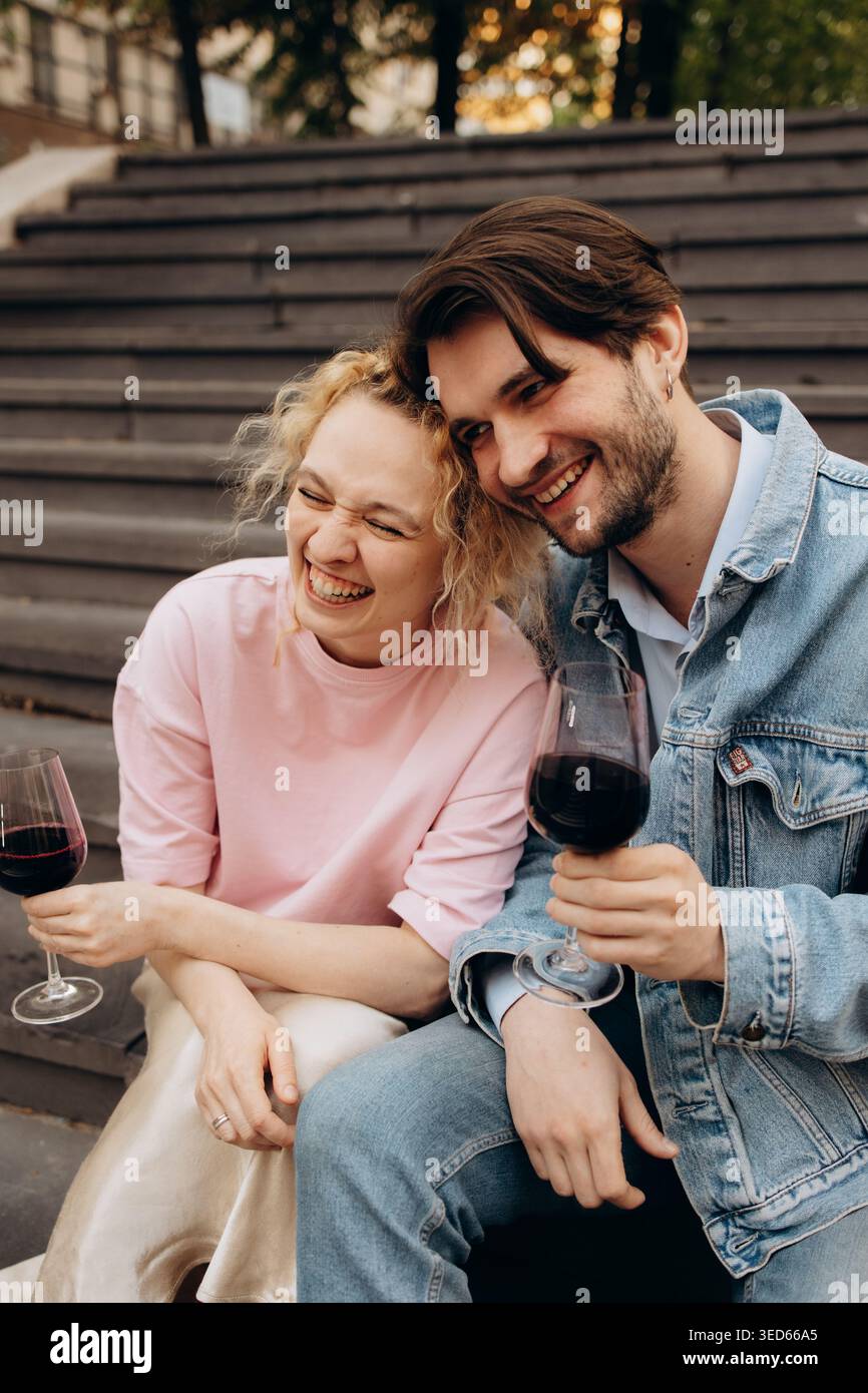 Happy young couple drinking red wine outdoors, laughing Stock Photo