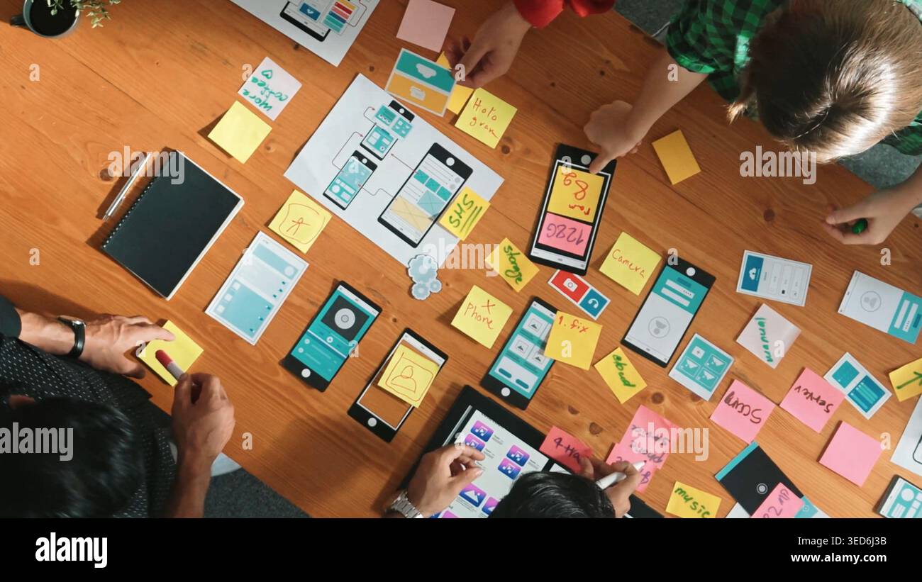 Top view of software developer team looking Ux Ui design for mobile phone interface from tablet while comparing and planning wireframe prototype Stock Photo