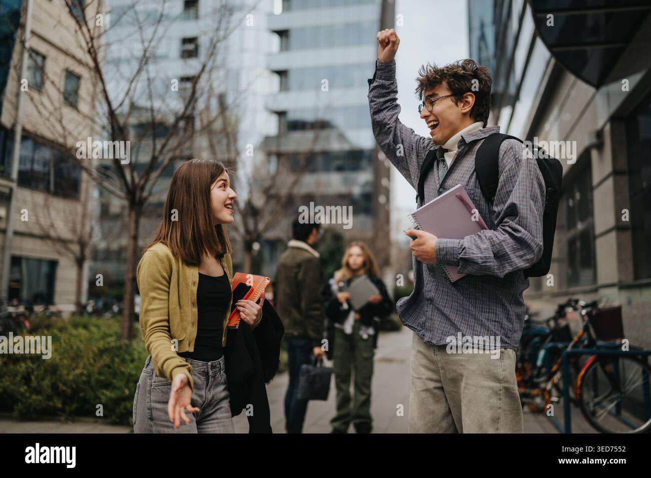 Students celebrating and talking on an urban campus walkway with backpacks and notebooks Stock Photo