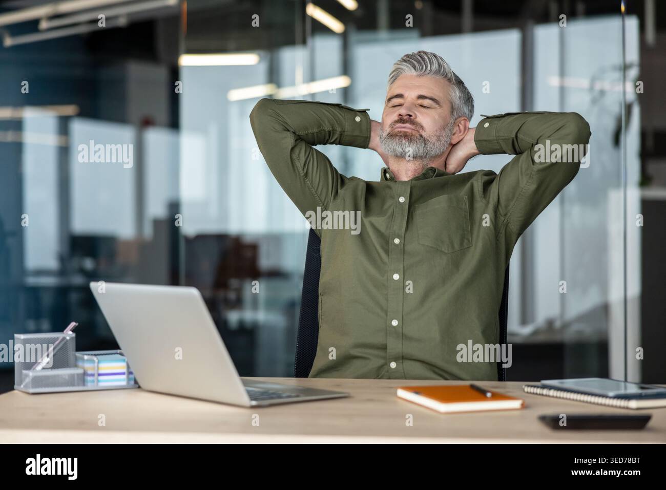 Mature businessman finding a moment of calm and peace, leaning back in his office chair with hands behind his head and eyes closed, taking a refreshing break from a busy workday Stock Photo