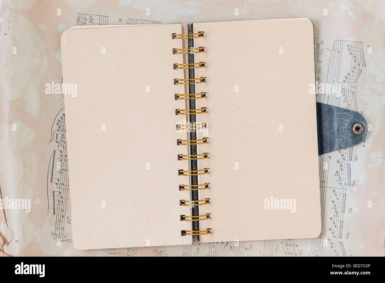 Flat lay of open notebook with spiral binding lies on sheet music, with blank pages ready for notebook layout, writing, journaling, study, or planner Stock Photo