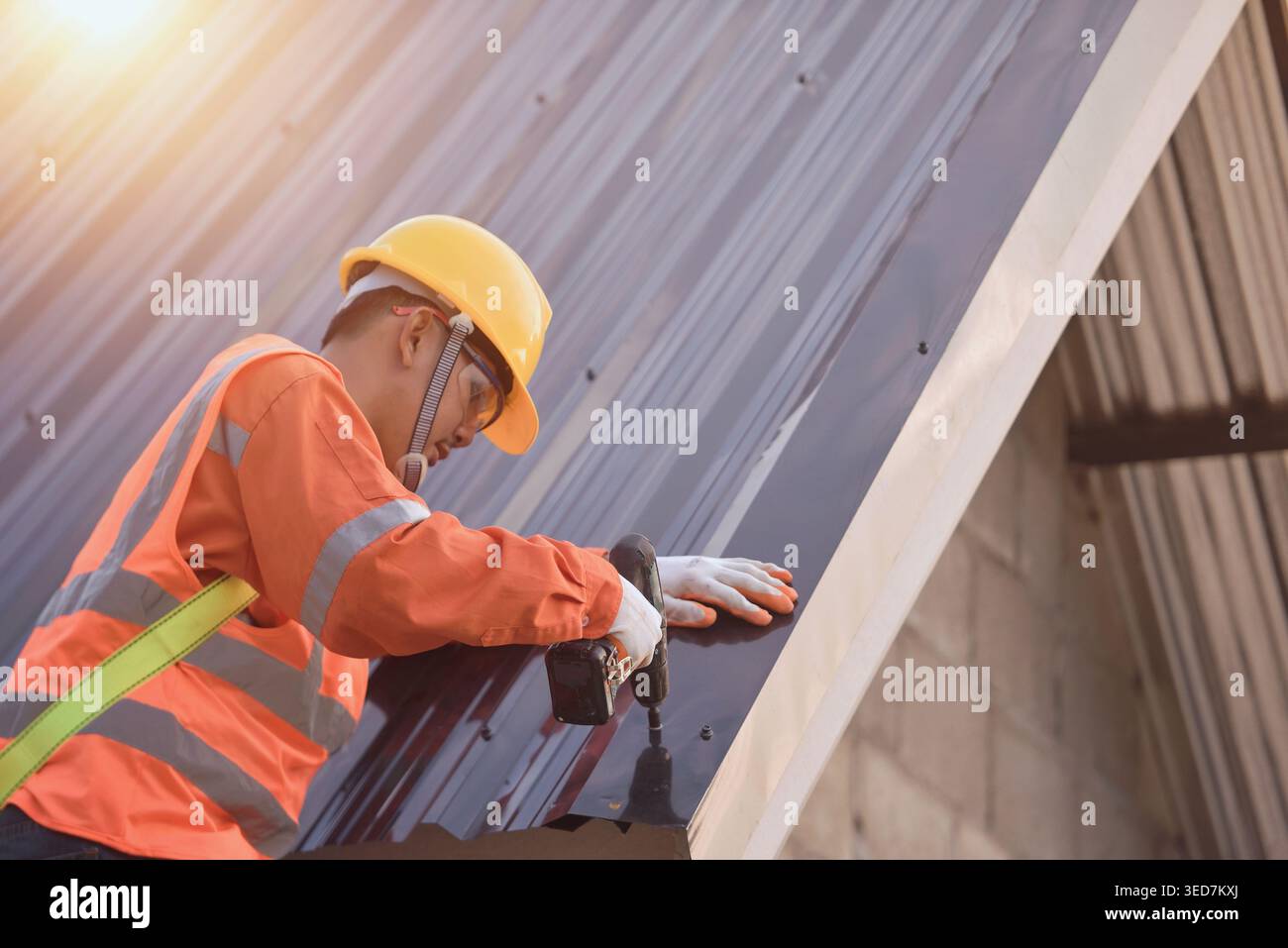 Side view of a Construction worker installing metal sheets on a roof, Thailand Stock Photo
