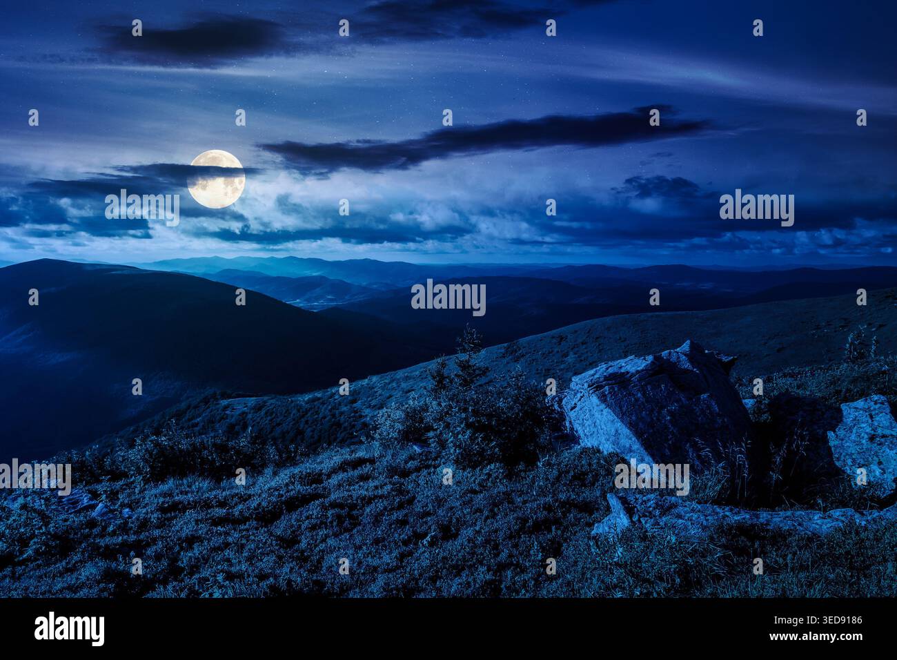 Carpathian mountain summer landscape at night. full moon over meadow with huge stones among the grass on top of the hillside near the peak of mountain Stock Photo