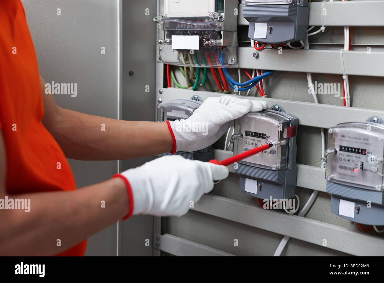 Electrician with screwdriver checking electrical meter indoors, closeup Stock Photo