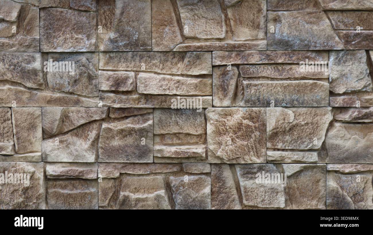 Wall decoration with square stone tiles of various sizes in grey-brown colour with a textured surface imitating the relief of natural stone is a decor Stock Photo