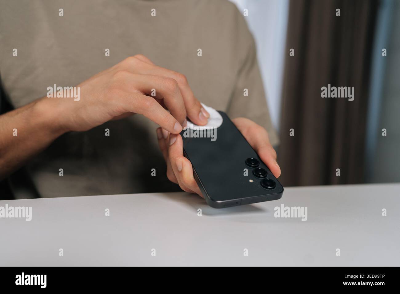 Close-up hands of man cleaning and disinfecting black smartphone with cotton pad, maintaining personal hygiene and device sanitation, preventing germ Stock Photo