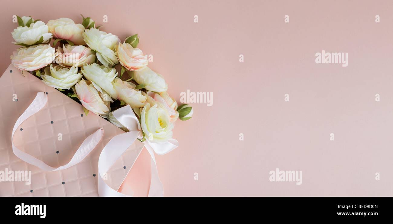 Festive composition featuring a quilted pink gift bag filled with cream and blush artificial rose flowers, accented by a white ribbon bow. Stock Photo