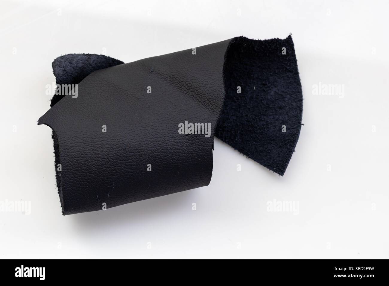 Folded Black Leather Piece Revealing Dark Suede Interior on White Background, Raw Genuine Material Close-Up Stock Photo