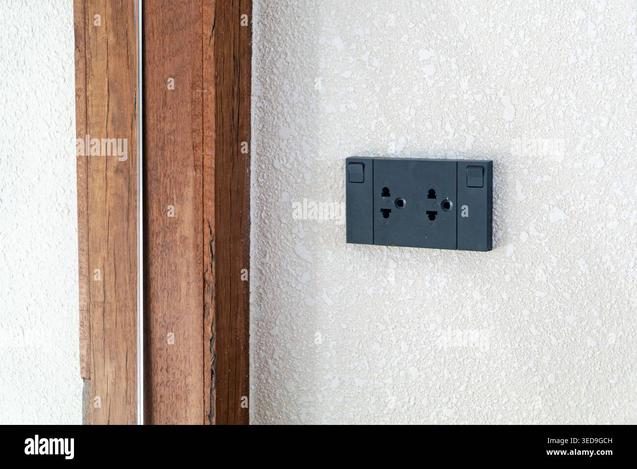 A sleek, modern wall socket installed on a white textured wall adjacent to a wooden panel, designed for easy access to electrical power in residential Stock Photo