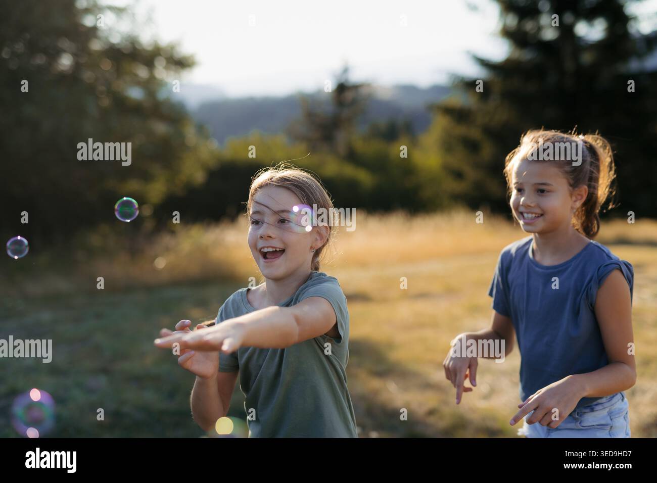 Two sisters blowing soap bubbles together in nature during spring day. Stock Photo