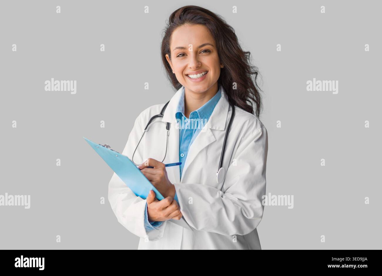 Portrait of smiling young doctor in uniform holding clipboard, looking and smiling at camera, grey background Stock Photo