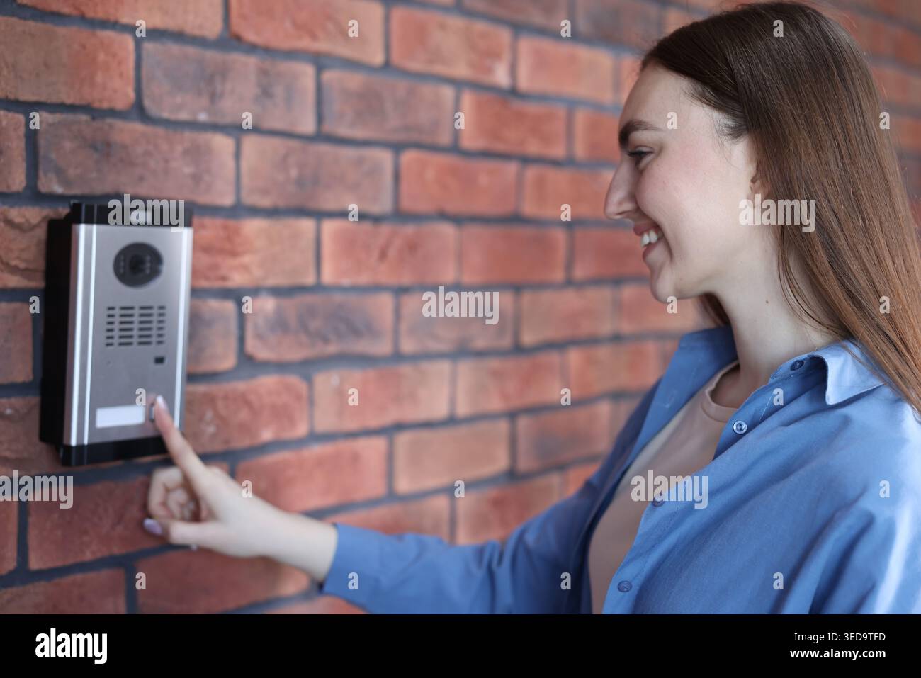 Woman pressing button on intercom panel near brick wall Stock Photo