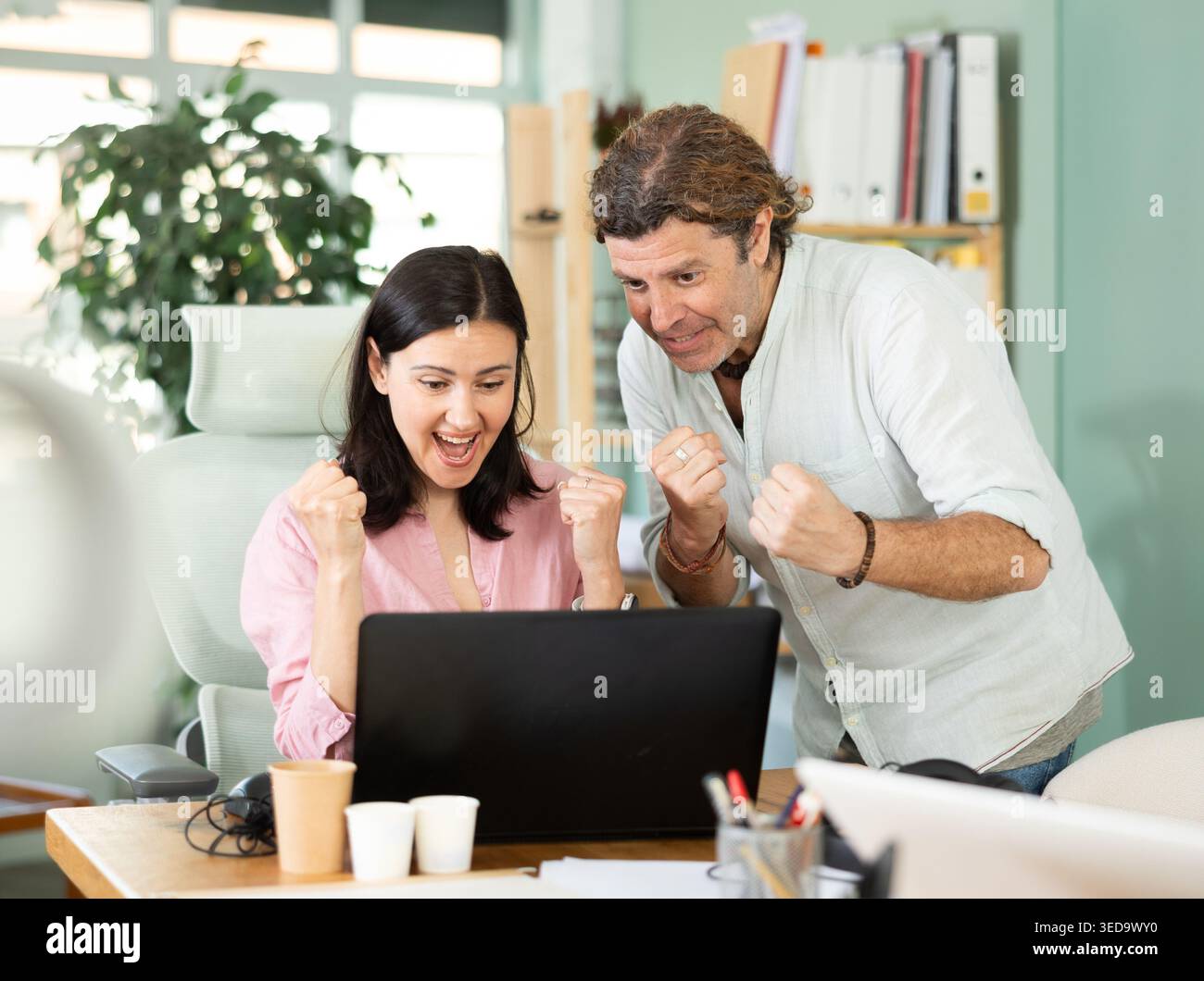 Happy colleagues sharing success while looking at laptop screen Stock Photo