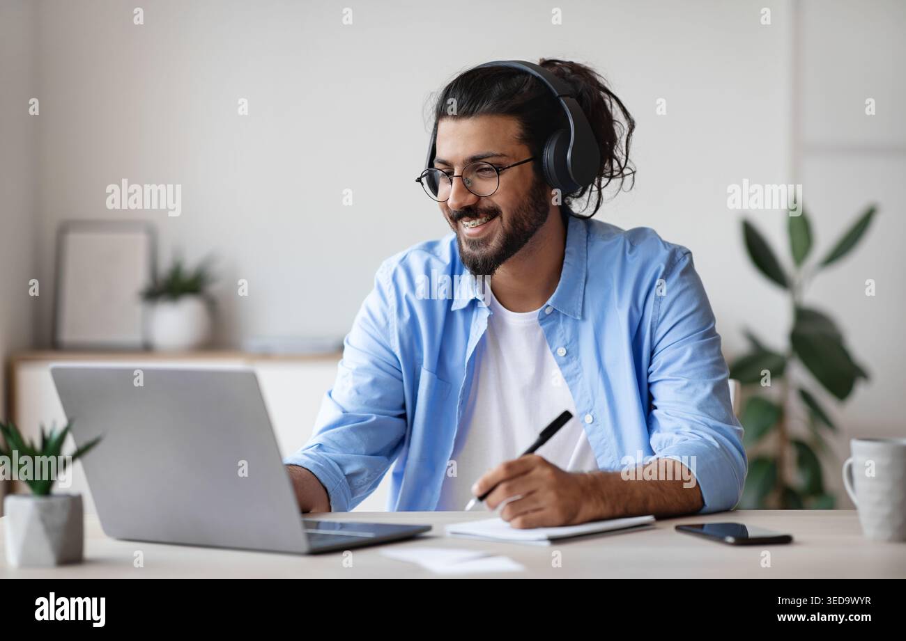 Distance Learning. Indian Guy Watching Webinar On Laptop Computer And Taking Notes Stock Photo