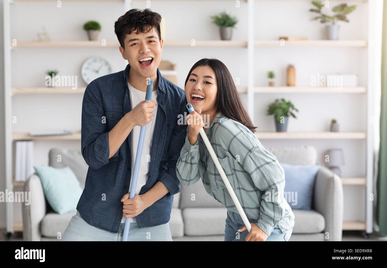 Positive chinese lovers having fun while cleaning house Stock Photo