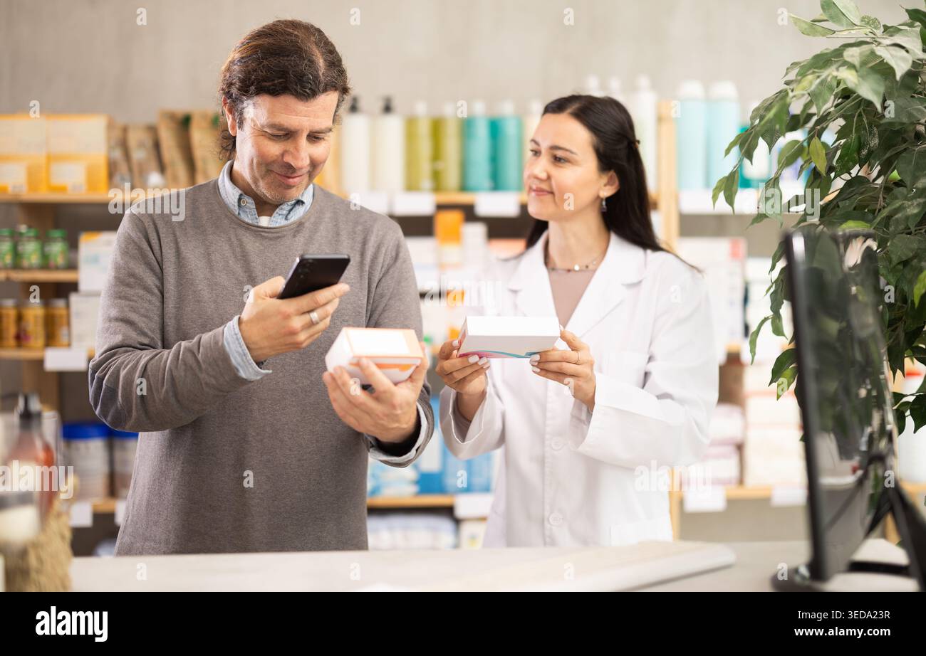 Middle-aged man scanning QR-code on pills box while pharmacist offering Stock Photo