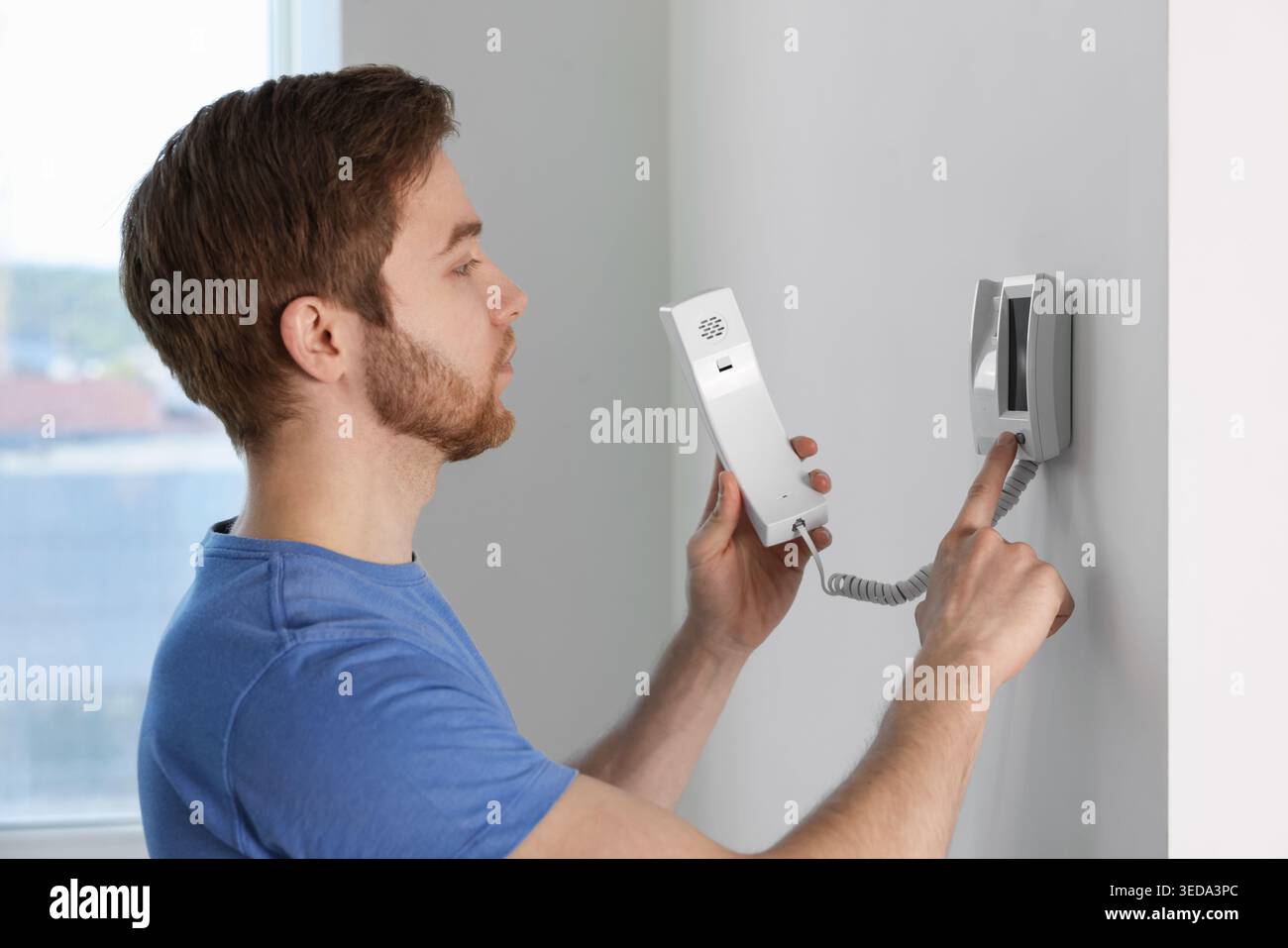 Man pressing button on intercom panel indoors Stock Photo