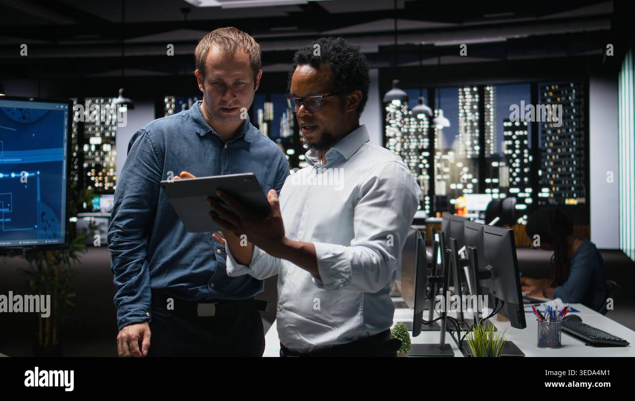 Teamworking tech startup coworkers using tablet, brainstorming ways to optimize performance in office. Technicians use machine learning on digital device for debugging, analyzing code Stock Photo