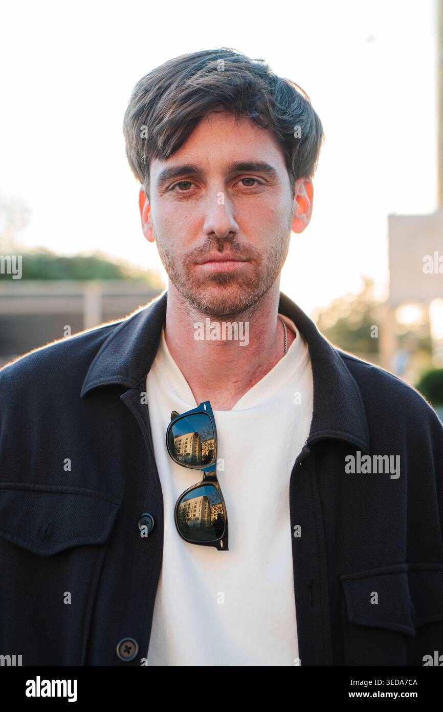 Thoughtful young adult man with sunglasses resting on his collar is gazing confidently with a serious expression, showcasing a moment of reflection Stock Photo