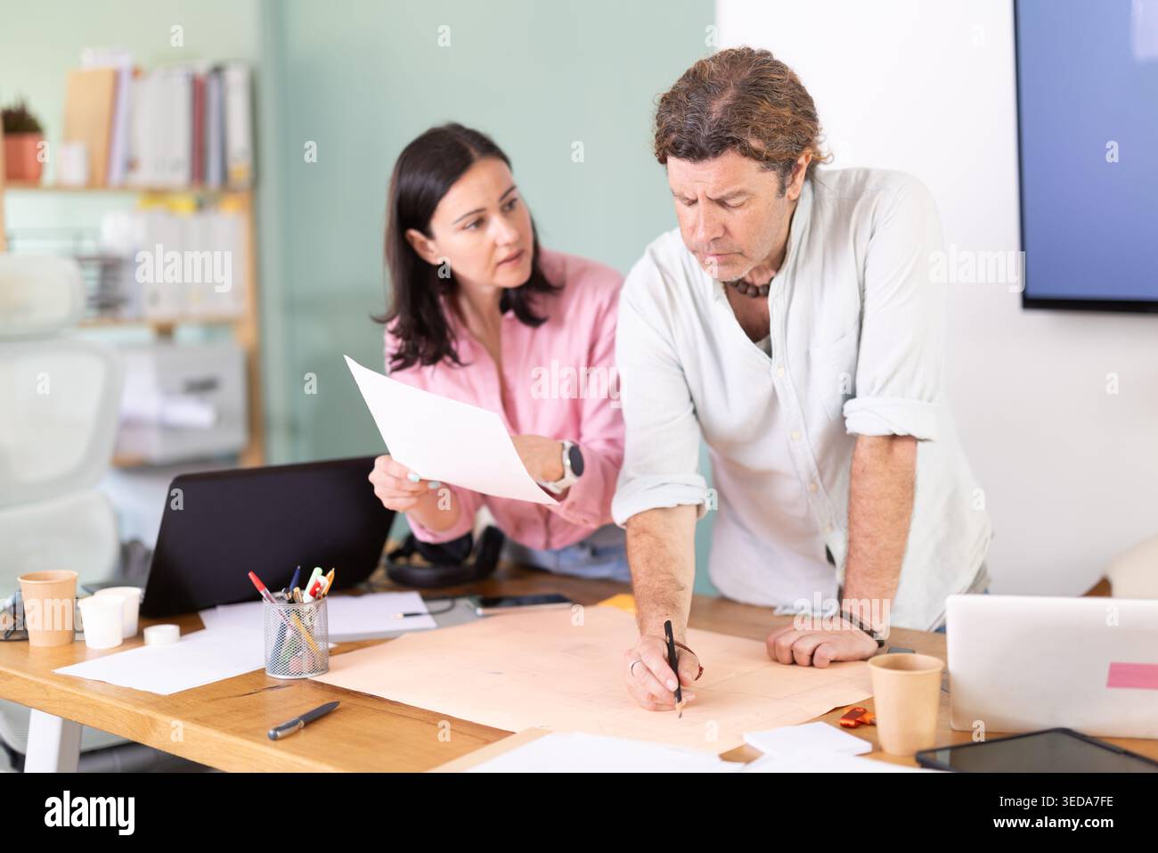 Middle-aged colleagues discussing construction plan leaning over office table Stock Photo
